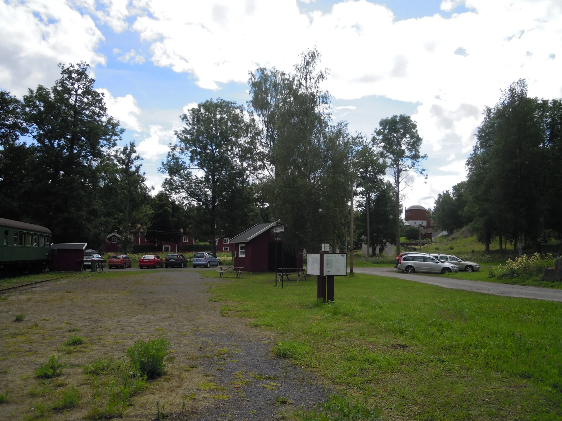 Grön bergsmansmiljö med röda byggnader, träd, väg och äldre industrilämningar i Pershyttan.