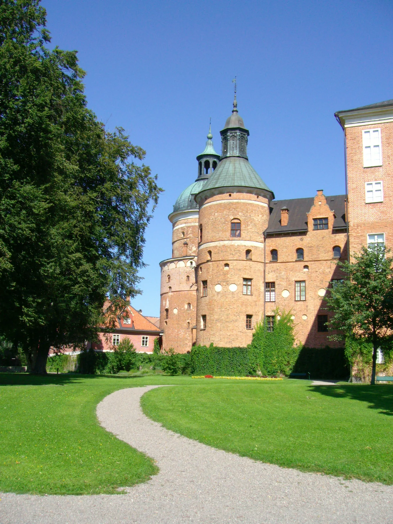 Gripsholms slotts runda tegeltorn bakom gröna träd och en slingrande grusgång.