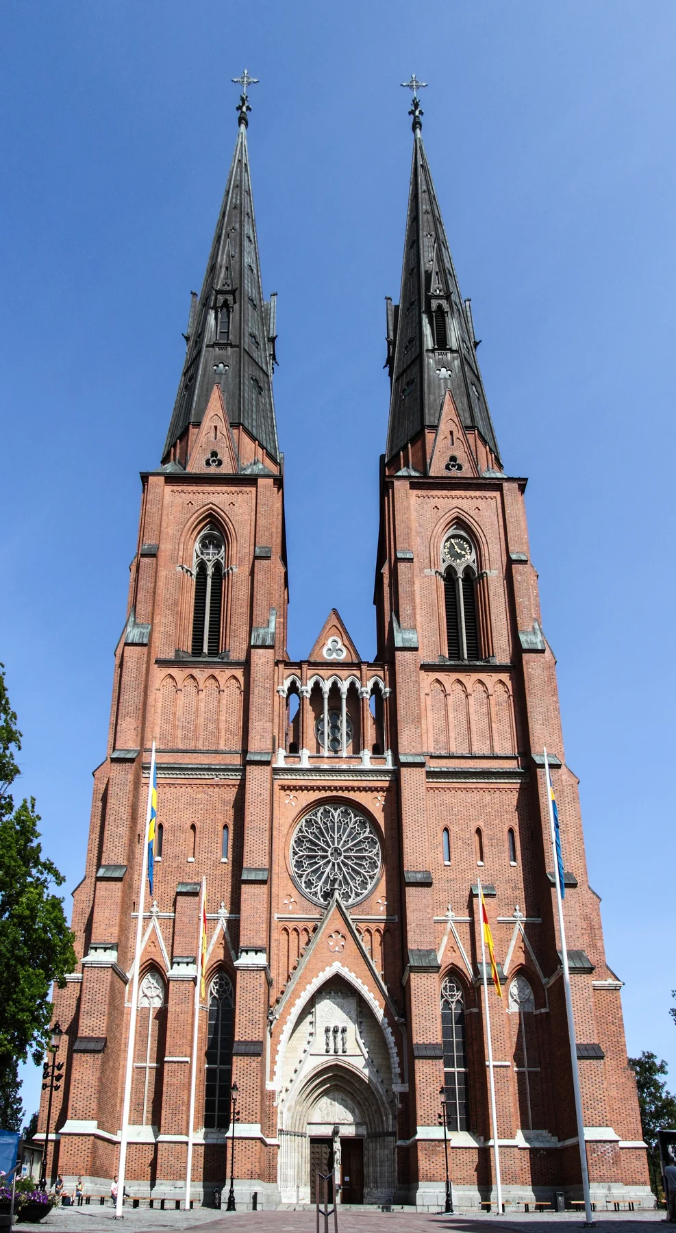 Uppsala domkyrkas röda tegelfasad med två höga mörka spiror mot klarblå himmel.