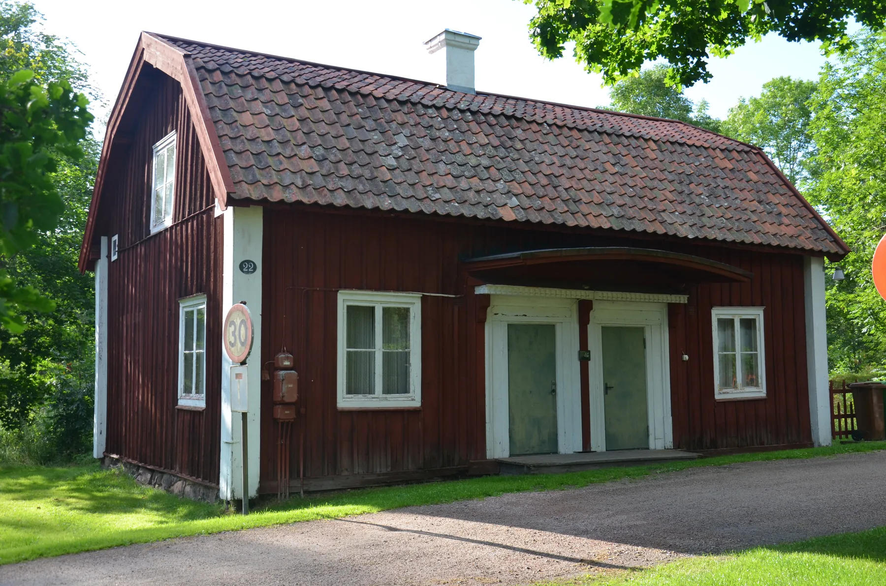 Rödmålat brukskontor med tegeltak och ljusa dörrar i grön bruksmiljö.